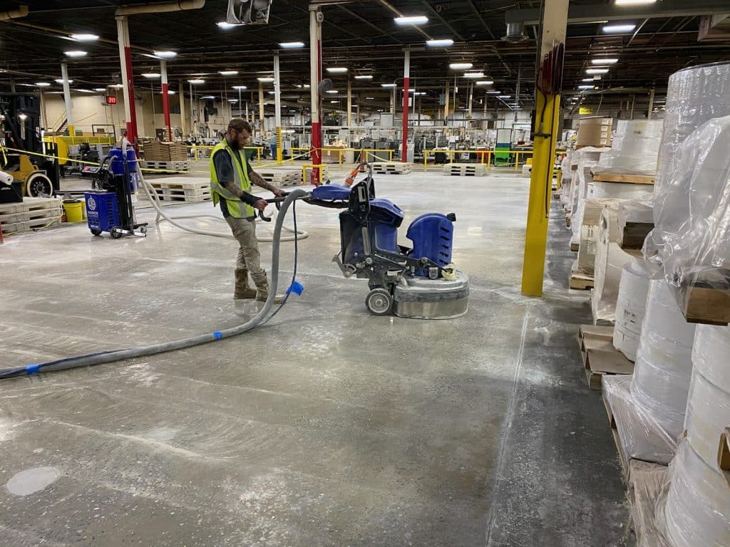 Image of a contractor using a large grinder to smooth and level a concrete floor surface, creating a uniform and level finish.
